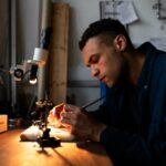 Engineer working with precision tools on electronic components in a well-lit workshop.