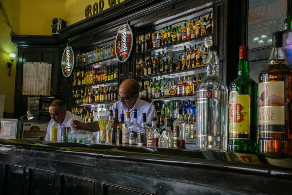 Explore a vibrant Havana bar with bartenders amidst a vast collection of liquors.